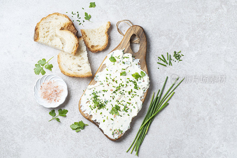 Simple green  butter board – trand of food blogger Tik Tok. Butter with fresh herbs: wild onion, parsley, rosemary and pink salt on a wooden board, gray stone background, rustic style. Simple and healthy snacks and aperitif, artisan bread , copy space